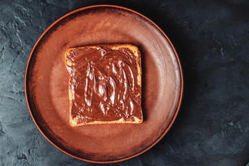 Toast with chocolate hazelnut cream in a brown plate on dark background, top view