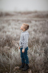 A boy with blond hair in the winter in the field looks up at the sky. Snow and frost in the park