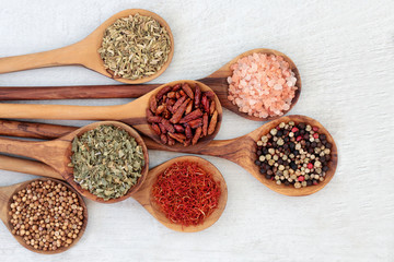 Herb and spice food seasoning in olive wood spoons with coriander seed, saffron, herbs de provence, peppercorns, chili peppers, himalayan salt and fennel. Left to right on rustic wood background. 