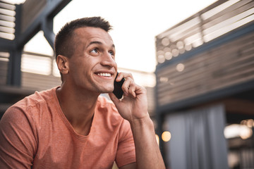 Positive man in T-shirt looking up while talking on the phone
