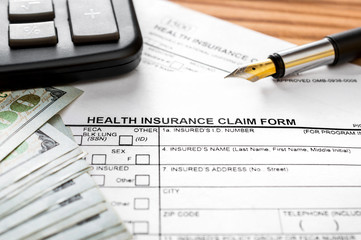 Health insurance claim form with calculator, money and pen on the table.