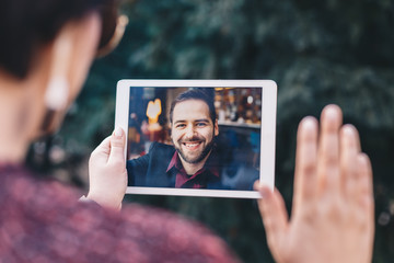 Young woman holding a tablet in her hands, having a video call chat with her freelancer boyfriend who is away on business trip. Concept of keeping long distant relationship in career oriented world. - obrazy, fototapety, plakaty