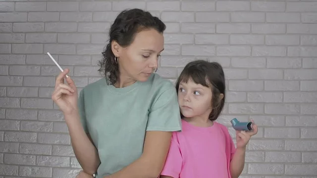 Smoking mother. Woman smokes with a child. The concept of smoking parents  is children of asmatics. Maths looks with a cigarette at her daughter with  an inhaler for an asmatic attack
