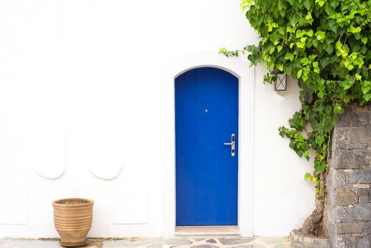 Traditional Greek blue door with white wall, plant and terra cota vase