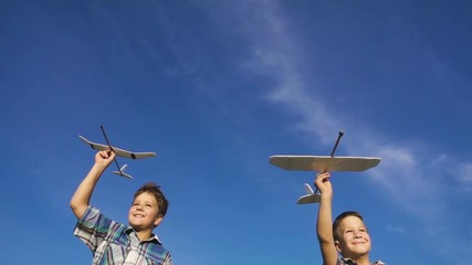 Two boys running with airplanes against blue sky