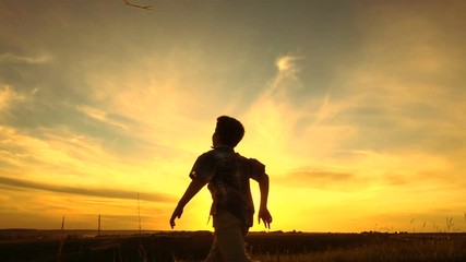 Silhouette of boy launching his airplane against sunset
