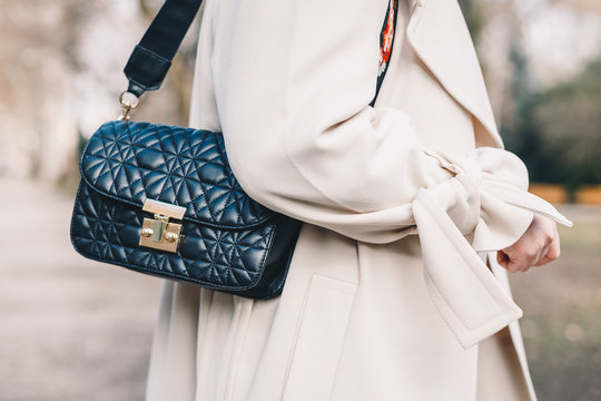 Close up of a black quilted purse hanging from the shoulder of a young woman wearing a white coat.