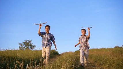 Two boys running with airplanes at the hill