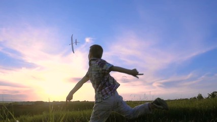 Silhouette of boy launching his airplane against sunset