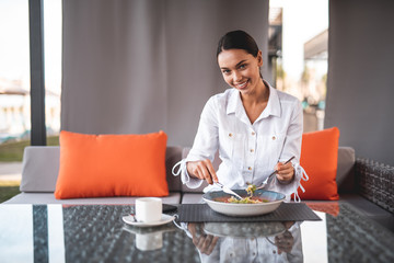 Waist up of positive smiling woman having lunch outdoors