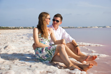 Fototapeta na wymiar Happy lovers on beach of pink lake. Smiling young woman and man in nature.