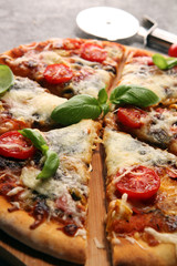 Vegetarian Italian pizza with melted cheese, red tomatoes and green basil on a table decorated by cheese, tomato and cherry tomatoes