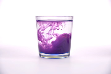 Glass with water on a white background with purple paint