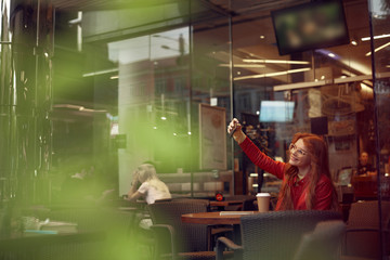 Attractive young lady in glasses making selfie in cafe