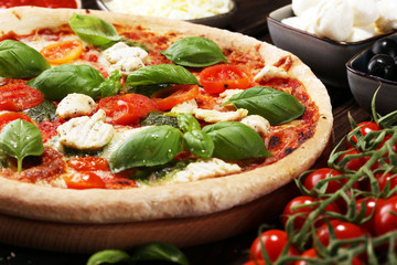Pizza with tomatoes, mozzarella cheese, black olives and basil. Delicious italian pizza on wooden pizza board.