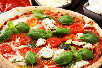 Pizza with tomatoes, mozzarella cheese, black olives and basil. Delicious italian pizza on wooden pizza board.
