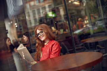 Beautiful red-haired girl reading book and smiling