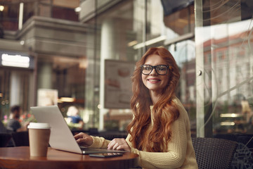 Beautiful red-haired girl using laptop in cafe