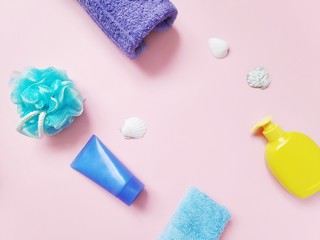 Flat lay beauty products, natural cosmetics for skincare. Blue sponge, purple terry towel, body cream, yellow liquid soap package and seashells on a pin background. Mockup, free space for text