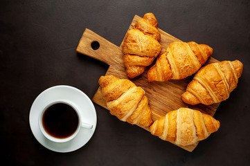 coffee and croissants on wooden cutting board, on the background concrete