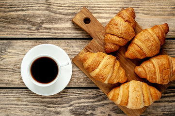 coffee and croissants on wooden cutting board, on wooden background