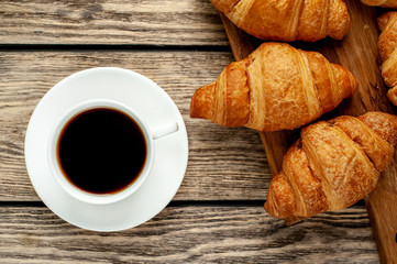 coffee and croissants on wooden cutting board, on wooden background
