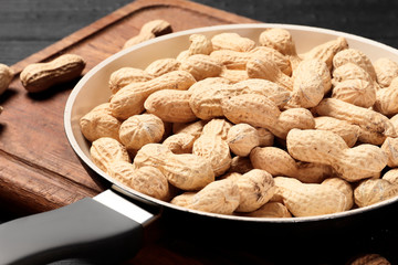 Roasted peanuts in a frying pan on the kitchen board on a wooden table. home serving. Place for text.