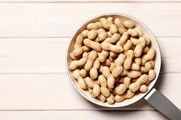Frying pan full of fried tasty peanuts on a white wooden background with place for text. Close-up.
