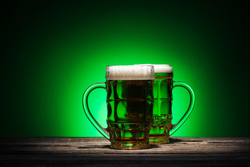 glasses of green lager standing on wooden table on green background