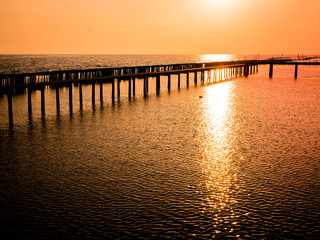 Naklejka na ściany i meble Low tide during sunset silhouette wooden pole and bridge through the sea beautiful orange sky background of nature