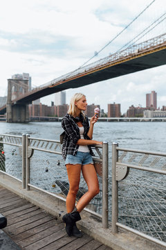 USA, New York City, Brooklyn, young woman standing at the waterfront eating an ice cream