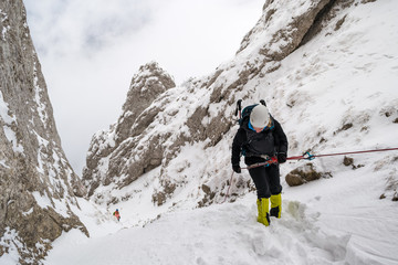 Female alpinist rappeling into a steep canyon filled with snow, during a Winter hiking trip, in Piatra Craiului mountains, part of the Carpathian mountains, in Romania.