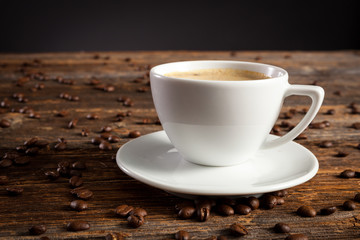 White cup of coffee with several coffee beans on standing on a vintage wooden table