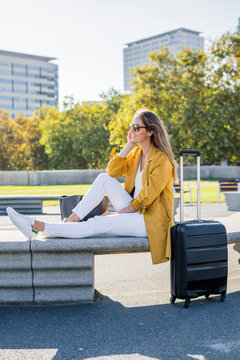 Smiling woman with suitcase sitting on a bench in the city