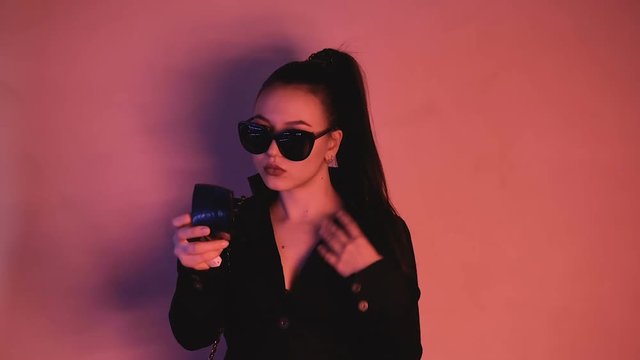 Brunette in neon lights. A woman with glasses and a black jacket paints her lips. HD