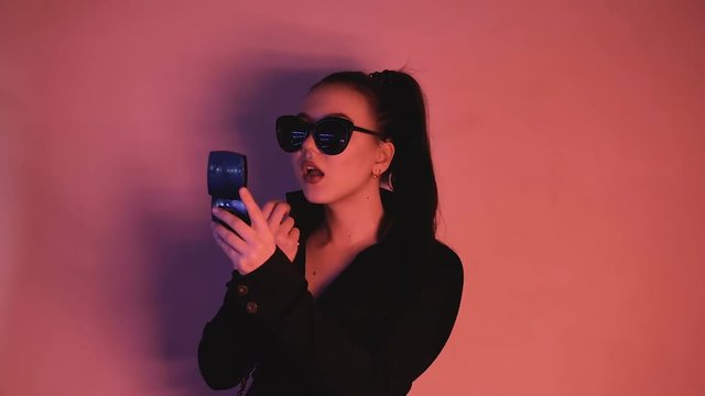 Brunette in neon lights. A woman with glasses and a black jacket paints her lips. HD