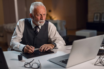 Senior businessman using graphic tablet while working on laptop in the office.