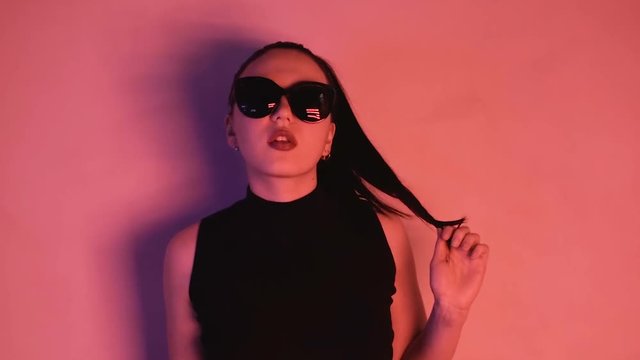 Brunette in neon lights. A woman in sunglasses and a black jacket looks into the camera. HD