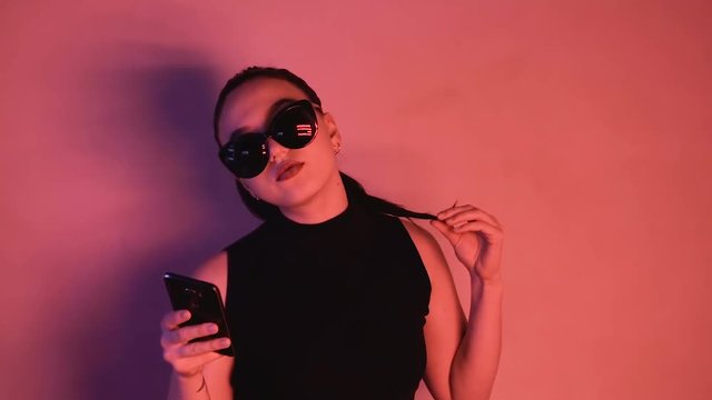 Brunette in neon lights. A woman in sunglasses and a black jacket looks into the camera. HD
