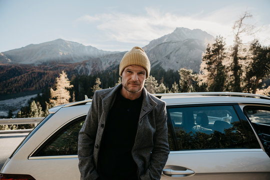 Man travelling through Switzerland, standing by his car