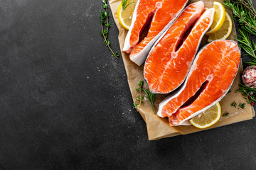 Fresh raw salmon fish steaks on black background with ingredients for cooking. Closeup. Top view