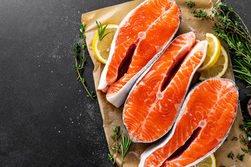 Fresh raw salmon fish steaks on black background with ingredients for cooking. Closeup. Top view