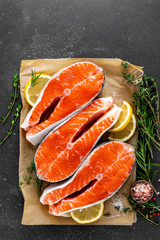 Fresh raw salmon fish steaks on black background with ingredients for cooking. Closeup. Top view