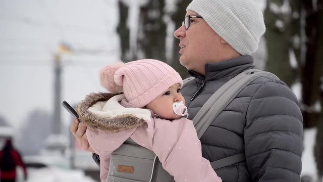 Working father with baby in carrier outdoors winter day talking phone 4k