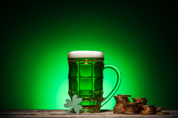 glass of green irish beer near golden coins and cube calendar on green background