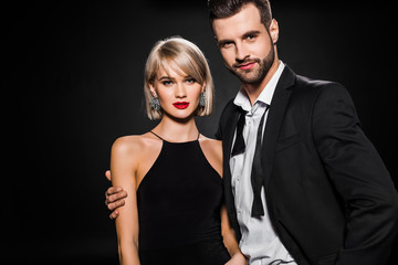 smiling bearded boyfriend hugging attractive elegant girlfriend isolated on black