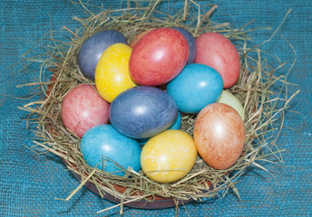 Easter eggs in a nest with hay on a blue canvas