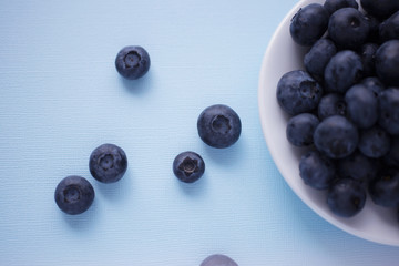 Fresh and juicy blueberries in white plate on blue background. Top view. Selective focus