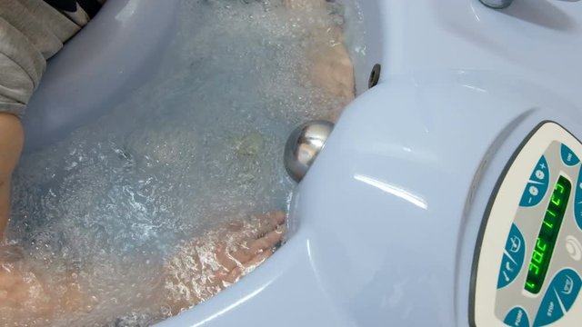 Closeup of female hands. Hydro massage of the upper limbs of an elderly woman in a therapeutic bubble bath.