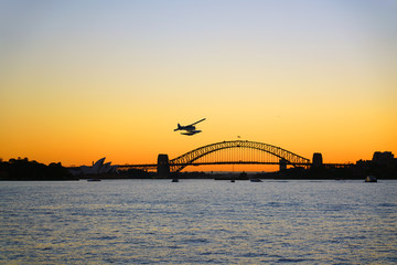 Sunset view of a seaplane flying in the orange sky by the iconic steel Sydney Harbour Bridge in New South Wales, Australia